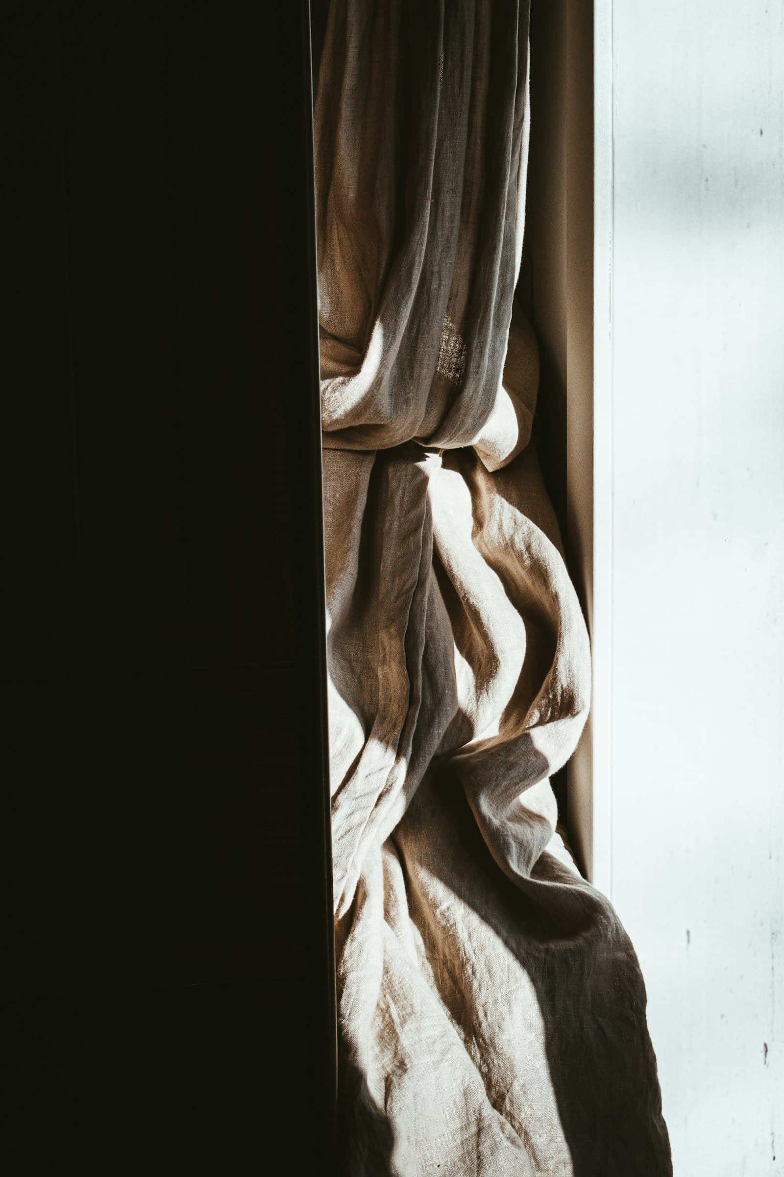 Beige cloth gathered into deep folds between a dark frame and a bright window.