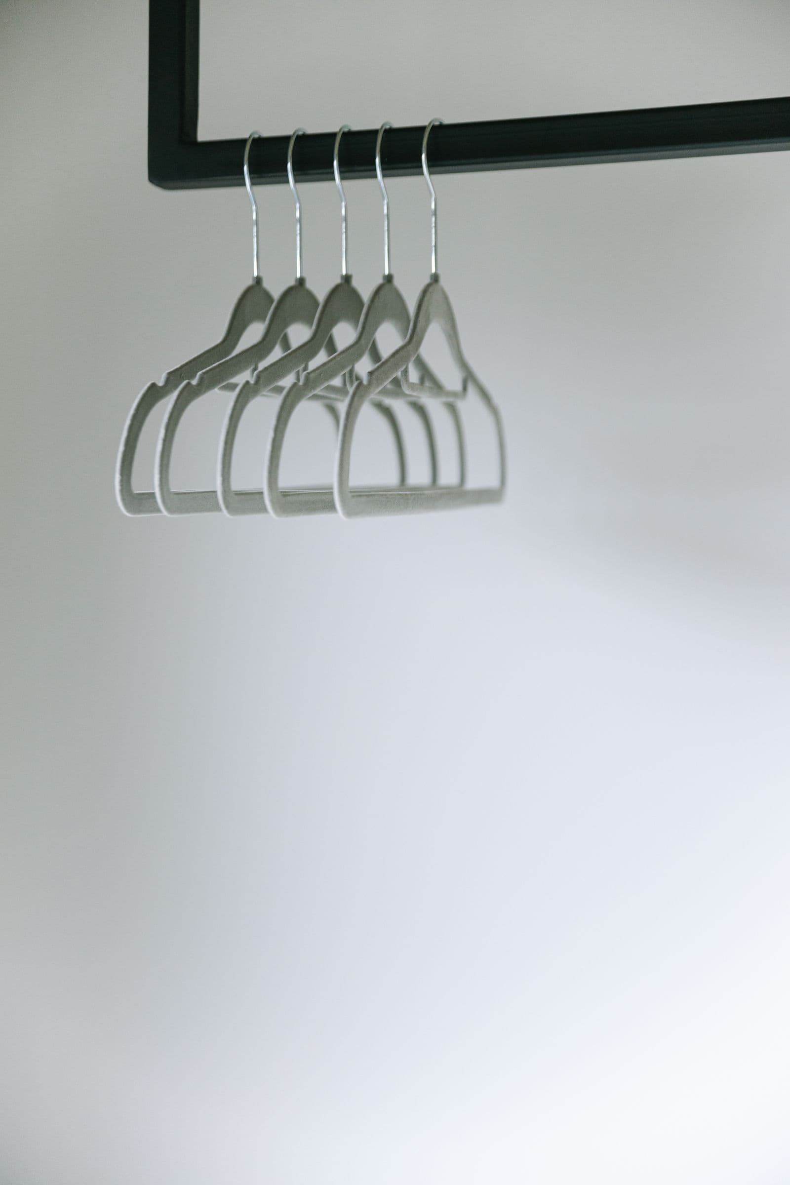 Empty grey clothes hangers on a rail against a pale wall.